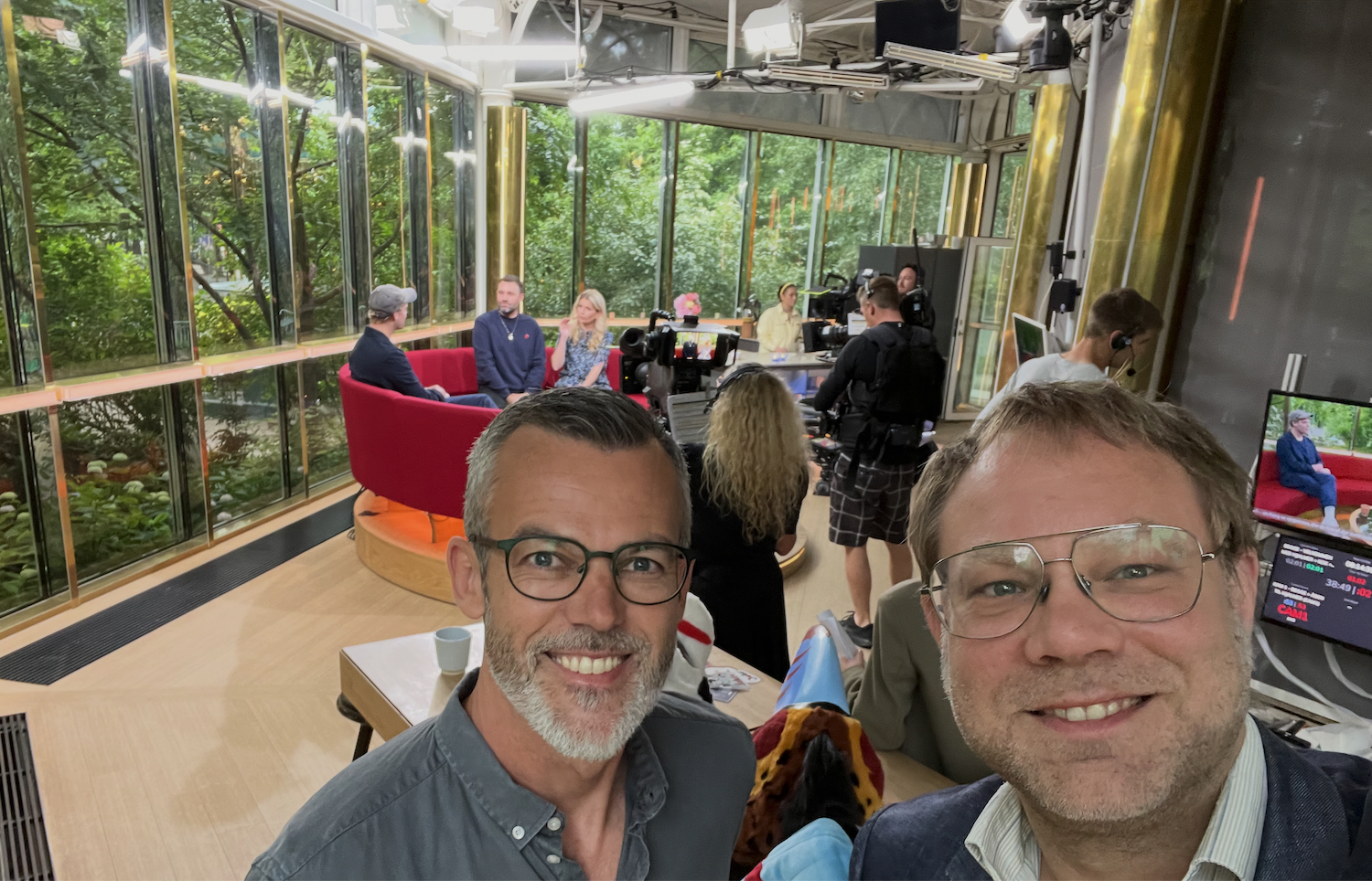 Selfie bag kulisserne i et tv-studie med kameraer og interviewområde i baggrunden